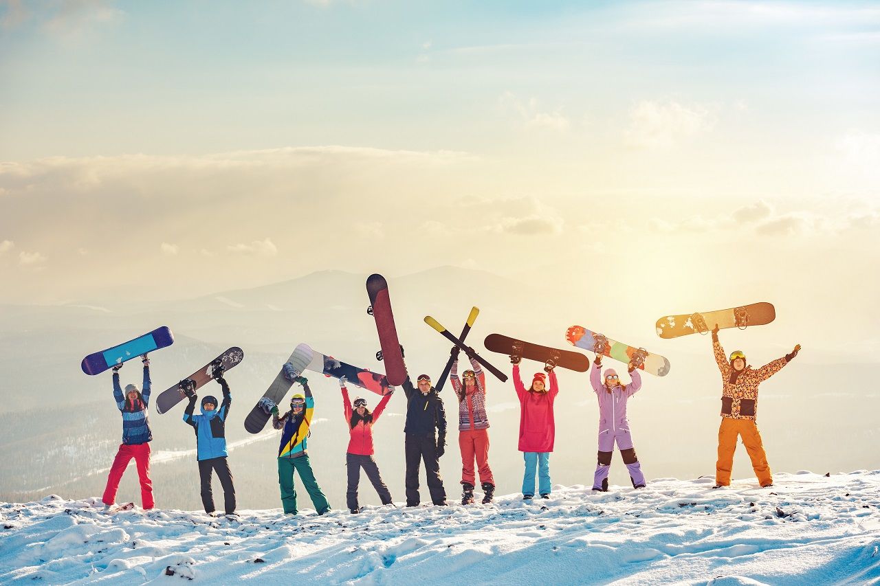 Eine Gruppe hält Skier und Snowboards in die Lüfte 